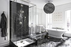 a black and white bathroom with a claw foot tub, marble flooring and chandelier