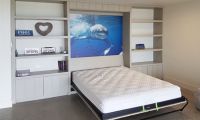 a bed sitting in the middle of a room next to a white book shelf filled with books