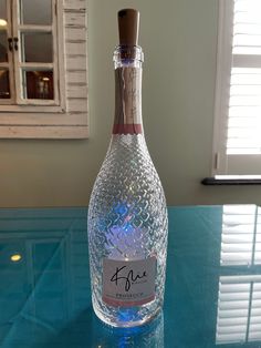 a bottle of wine sitting on top of a blue glass table next to a window