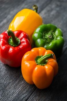 three different colored peppers sitting on top of a wooden table