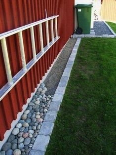 there is a red wall and some rocks in the grass next to an orange building