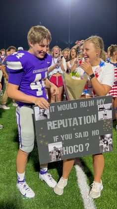 a couple of people standing on top of a field with a sign that says it would run my reptation if you said no hoco?