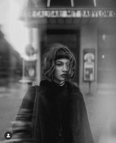 a black and white photo of a woman standing in front of a movie theater sign