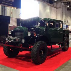 an old green truck is on display in a showroom with red carpet and white walls