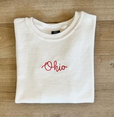 a white sweater with the word ohio embroidered on it, sitting on a wooden floor