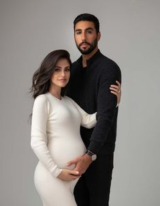 a pregnant couple posing for the camera in their white and black photoshoots with grey background