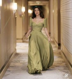 a woman in a green dress is walking down the hallway with her hand on her hip