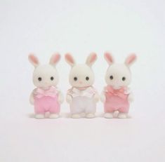 three small figurines are standing next to each other on a white surface, one is wearing a pink dress