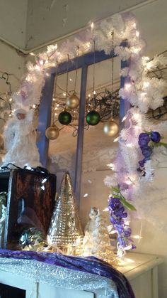 a white mantle with ornaments and lights on it in front of a mirror that is hanging from the wall