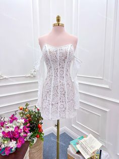 a mannequin with a white dress on display in front of flowers and books