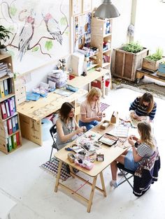 three women sitting at a table working on crafts in a room with lots of shelves