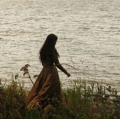 a woman in a long dress standing by the water