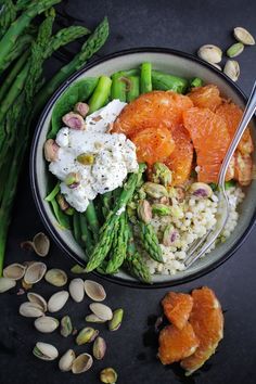 a bowl filled with asparagus, oranges and other food on top of a table