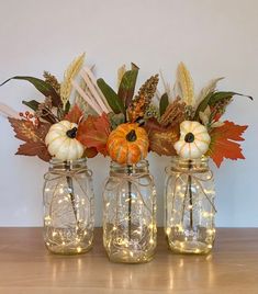 three mason jars filled with pumpkins, leaves and other fall decorations on a table