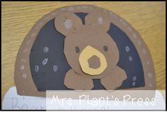 a brown teddy bear sitting on top of a wooden table next to a paper plate