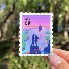 a person holding up a stamp with the silhouette of two people on it in front of some trees