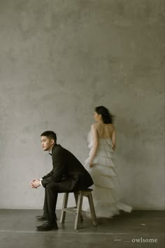 a man sitting on a stool next to a woman in a white dress and black suit