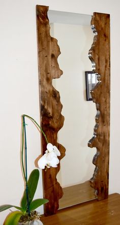 a vase with flowers sitting next to a mirror on top of a wooden table in front of a white wall