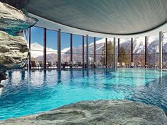 an indoor swimming pool with mountains in the background and large glass windows on both sides