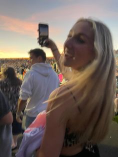 a woman with long blonde hair is holding up her cell phone at an outdoor concert