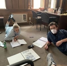 two people sitting on the floor with papers and pens in front of them, one person wearing a face mask