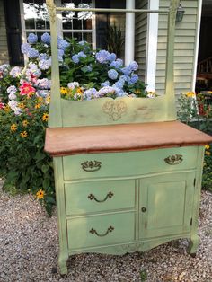 an old green dresser with a mirror on it's top and flowers in the background