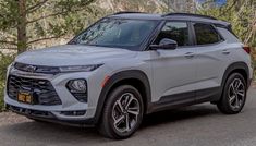 a silver chevrolet suv parked on the side of a road in front of some trees