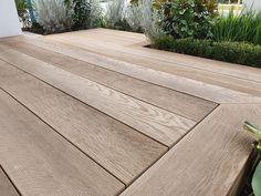 a close up of a wooden deck with plants in the background