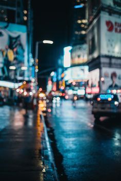 a city street at night with cars and people walking on the sidewalk in the rain