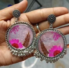 a pair of earrings with pink and red flowers on them are being held in someone's hand