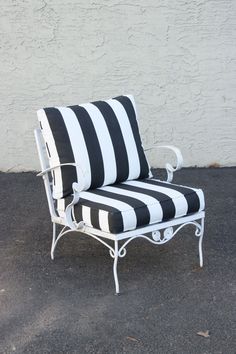 a black and white striped chair sitting in front of a white stucco wall with an iron frame