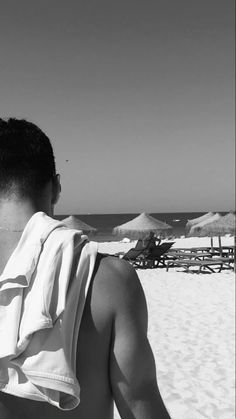 a man sitting on top of a sandy beach next to the ocean and umbrellas