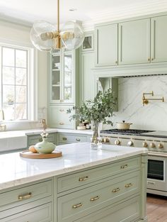 a kitchen with green cabinets and marble counter tops, an island in front of the stove