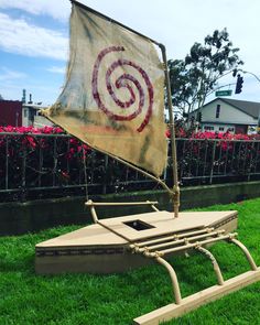 a wooden boat sitting on top of green grass next to a red and white flag