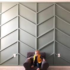 a small child sitting on a chair in front of a wall with geometric panels behind it