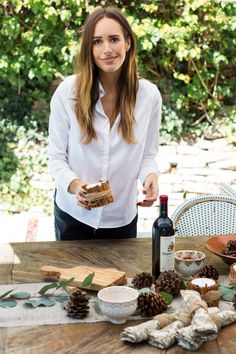 a woman holding a piece of cake next to a bottle of wine and pine cones