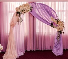 a wedding arch decorated with flowers and purple drapes in front of a curtained window