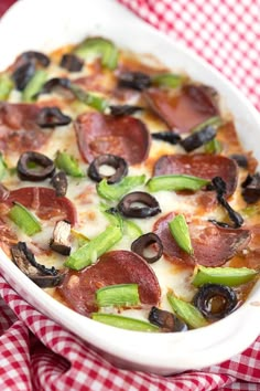 a pizza with pepperoni, green peppers and olives in a white casserole dish