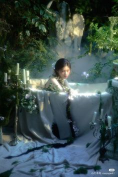 a woman sitting in a bathtub surrounded by greenery and candles with flowers on it