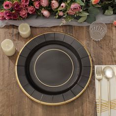 a black plate with gold trim sits on a wooden table next to candles and flowers