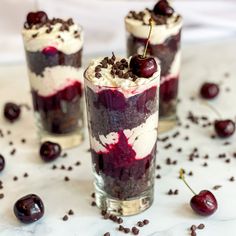 three desserts with cherries and whipped cream in them on a white tablecloth