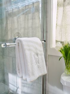 two towels are hanging on a towel rack in the bathroom, next to a vase with tulips