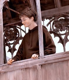 a young man wearing glasses is looking out from an old wooden building window sill