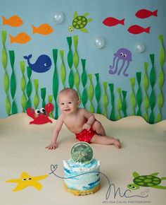 a baby is sitting in front of a cake with an ocean theme on the wall