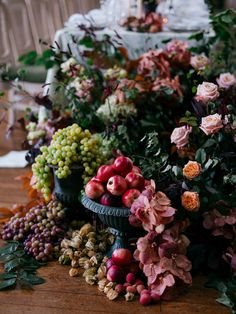 an arrangement of flowers, fruit and leaves on a table with a candle in the background