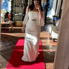 a woman in a white dress taking a selfie with her cell phone while standing on a red carpet