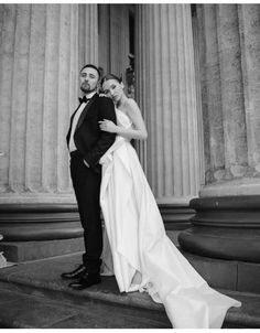 a bride and groom pose for a photo in front of the columns of an old building