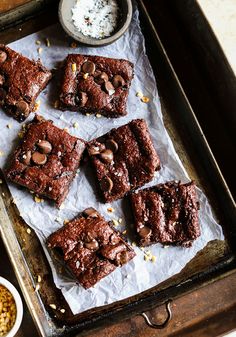 chocolate brownies on parchment paper with bowls of nuts