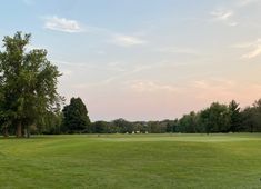 a green field with trees in the background and people playing golf on the other side