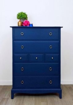 a blue dresser with two vases on top and one potted plant sitting on top